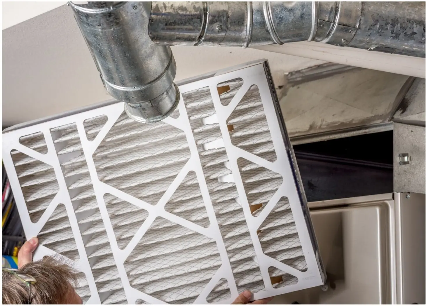 Furnace air filter being removed beneath supply ductwork