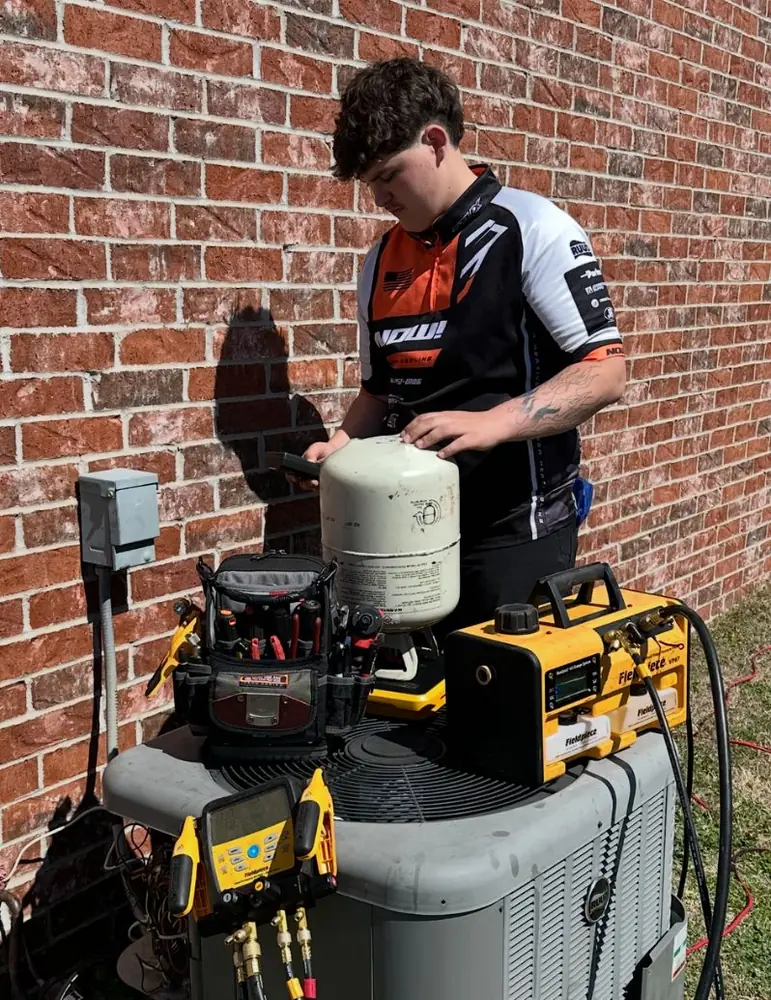Technician recovering refrigerant from an outdoor AC unit with gauges and a recovery tank